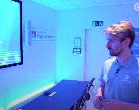 Video-Vorschaubild eines Mannes, der sich einen Microsoft Teams Signature Room mit Q-SYS Peripheriegeräten ansieht