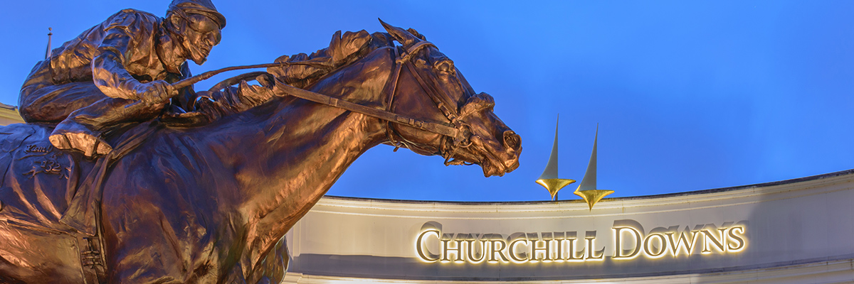 Schild des Churchill Downs Gebäudes mit einer bronzenen Statue eines Jockeys auf einem Pferd im Vordergrund